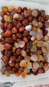 Bulk polished heart-shaped agate stones in warm amber and orange tones on a white tray