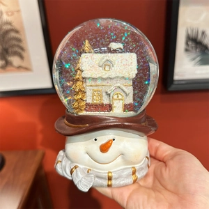 Close-up of a Christmas snowman snow globe music box featuring a golden tree and house