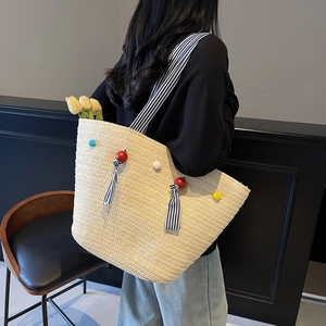 Handwoven beige straw tote bag with colorful pom-poms and striped straps for beach vacation