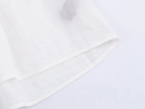 Detailed macro shot of white poplin shirt hemline with clean stitching and woven texture