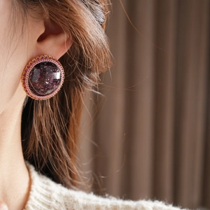 Close-up of circular resin stud earring with purple faceted stone and gold texture