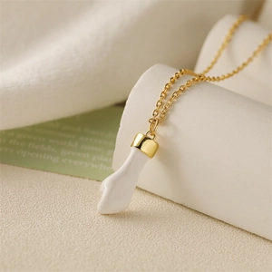 Golden necklace with a white enamel curved claw pendant on a soft textured background