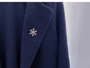 Close-up of sparkling rhinestone snowflake brooch pinned on deep blue wool coat collar