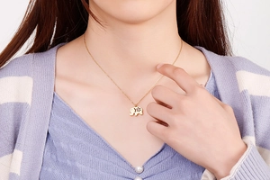 Detail shot of a golden elephant pendant necklace with floral cutout on a model neck