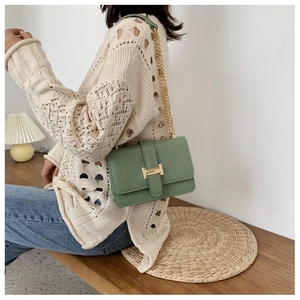 Detail of green crocodile texture shoulder bag with gold H clasp on a wooden bench