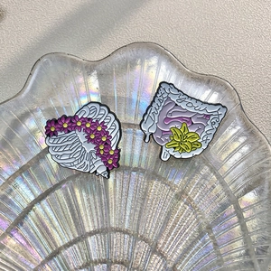 Artistic heart rib and gut enamel pins with purple flowers on iridescent shell tray