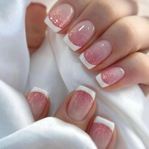 Close-up of French tip press-on nails with pink glitter gradient and white square tips