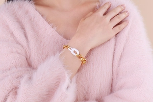 Détail d'un bracelet chaîne or et résine blanche porté avec un pull en mohair rose