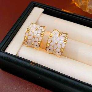 Gros plan de créoles en C plaquées or avec motif floral en émail blanc dans un écrin à bijoux