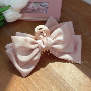 Vue détaillée d'une pince à cheveux en satin rose avec grand nœud sur table en bois