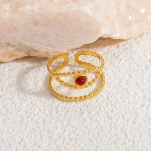 Detail shot of a double-layered gold ring featuring a round red stone on a stone surface
