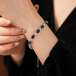 Detail of silver bracelet with oval dark blue gemstone and white zircon clover on wrist