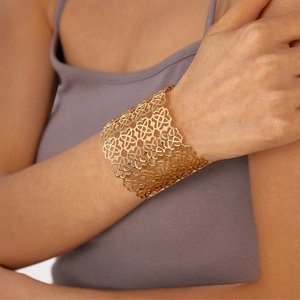 Dettaglio di un bracciale rigido dorato a fiori geometrici traforati indossato dal modello