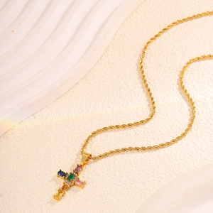Macro shot of gold rope chain and cross pendant with colorful gemstones on a textured surface