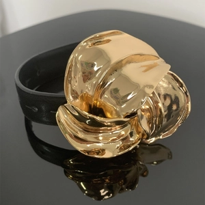 Modieuze zwarte leren armband met goudkleurige metalen bloem op een spiegeloppervlak