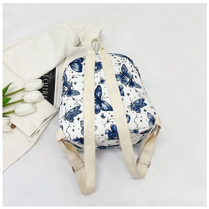 Detailed view of white backpack with blue butterfly pattern and golden hardware accents