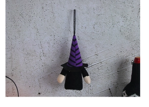 Hanging Halloween gnome ornament with purple striped hat and black body on concrete wall
