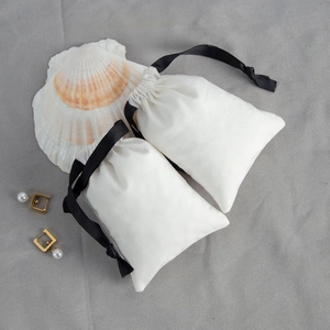 Detail of white cotton jewelry drawstring pouch with black ribbon and golden pearl earrings