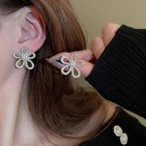 Close-up of silver hollow flower stud earrings with sparkling crystals worn by a model