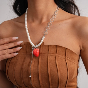 Detail of asymmetrical necklace with white pearls, silver rings, and a red strawberry charm