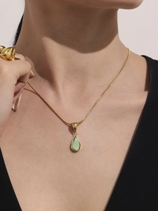 Détail d'un pendentif goutte dorée avec pierre verte sur un mannequin avec bague lave