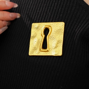 Macro detail of a vintage square golden brooch with hammered texture on black knitwear