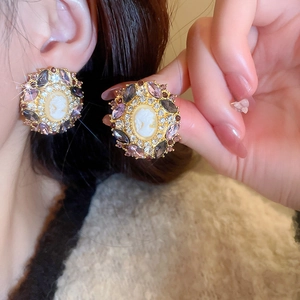 Detail of vintage gold cameo earrings with purple crystals and embossed portrait