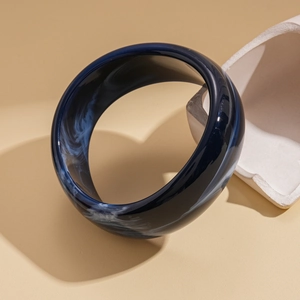 Detail of dark blue acrylic bangle with white marble texture on a white stone prop