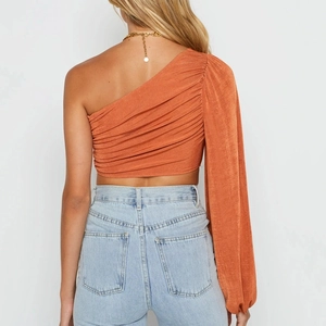 Vue détaillée du crop top orange à une épaule montrant les plis des manches et le dos ajusté