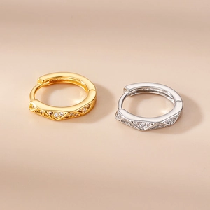 Macro detail of gold and silver hoop earrings with zircon stones on beige background