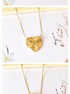 Macro detail of a 3D heart pendant necklace with a sleek gold snake chain on aesthetic paper