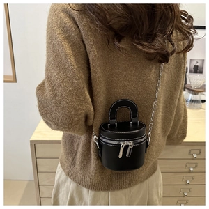 Détail d'un sac cylindre noir avec coutures blanches et bandoulière chaîne argentée