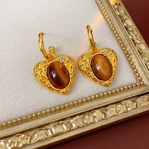 Detail of vintage heart earrings with brown oval resin and crystal on a beige tray
