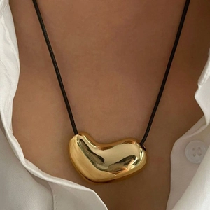 Close-up of a glossy gold abstract heart pendant on a black cord necklace worn on a model