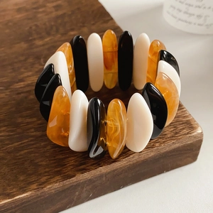 Detail of a geometric resin stretch bracelet in amber, black, and white on a wood base