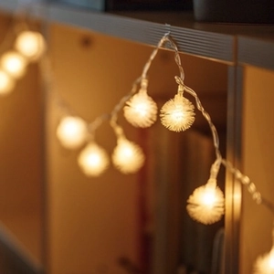 Warm white LED pom pom string lights hanging on wooden furniture for cozy home decor