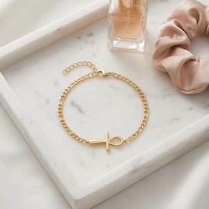 Golden Ankh cross bracelet displayed on a white marble tray with silk and perfume decor