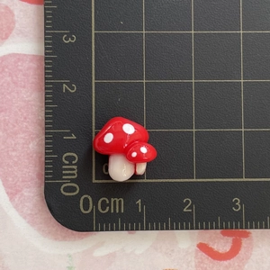 Detailed view of a 1cm red and white glass mushroom charm on a scale cutting mat