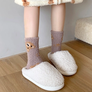 Close-up of fuzzy coral fleece socks with cute purple bear and white plush slippers