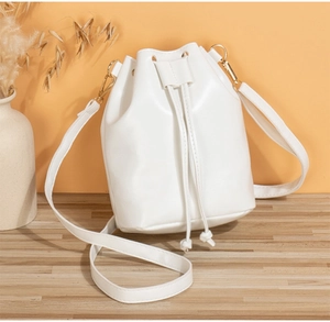 Detail of white mini bucket bag with drawstring closure on a warm minimalist background