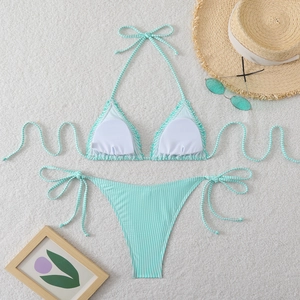 Flat lay of mint green striped bikini set with straw hat and sunglasses on white rug