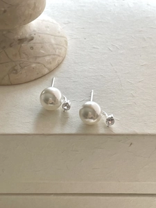 Detail view of silver pearl and zircon stud earrings on a textured background