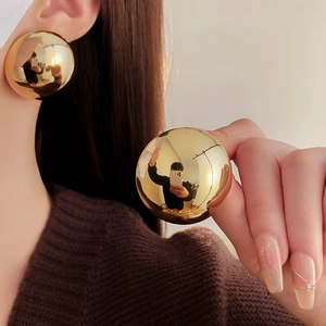 Macro shot of large polished gold sphere earrings showing metallic mirror finish