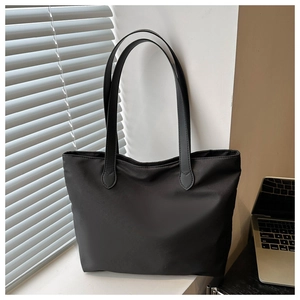 Detail of a black nylon tote bag with leather straps on a desk with laptop