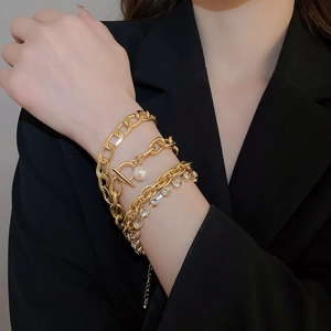 Detail of four-piece gold link chain bracelet set with pearl and rhinestones on black sleeve