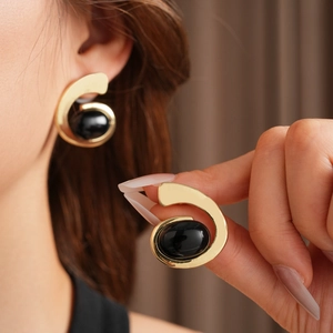 Gros plan de boucles d'oreilles spirales dorées avec pierre noire sur un modèle