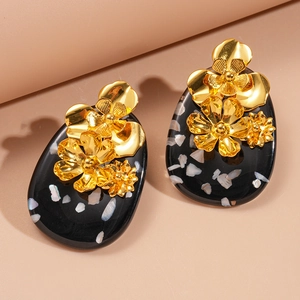 Detail shot of black resin oval earrings with gold floral accents and shell inlays