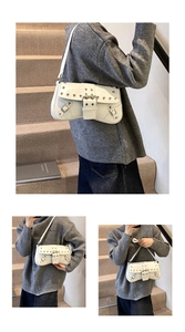 Macro detail of white faux leather shoulder bag featuring silver rivets and buckle straps