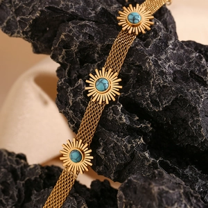 Detail of 18K gold-plated layered chain bracelet featuring turquoise sunflower charms