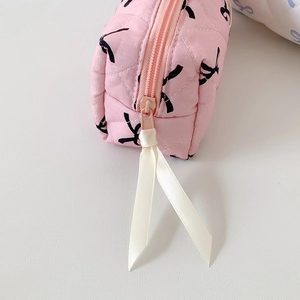 Close-up of pink quilted makeup bag showing metal zipper and black bow print texture